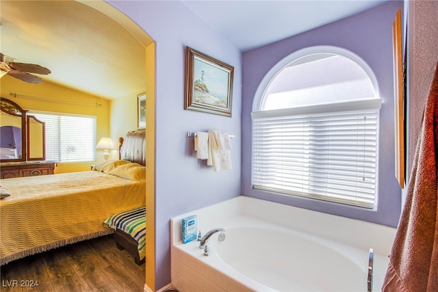 bathroom featuring lofted ceiling, tiled tub, wood-type flooring, and ceiling fan