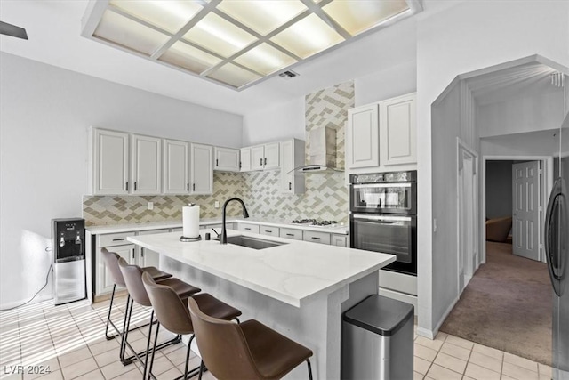 kitchen featuring wall chimney exhaust hood, a breakfast bar, light tile patterned floors, a kitchen island with sink, and sink