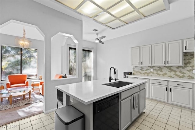 kitchen featuring sink, black dishwasher, ceiling fan with notable chandelier, backsplash, and a kitchen island with sink