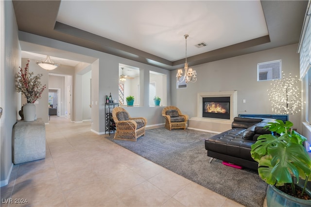 living room with light tile patterned floors, baseboards, visible vents, a tray ceiling, and a glass covered fireplace