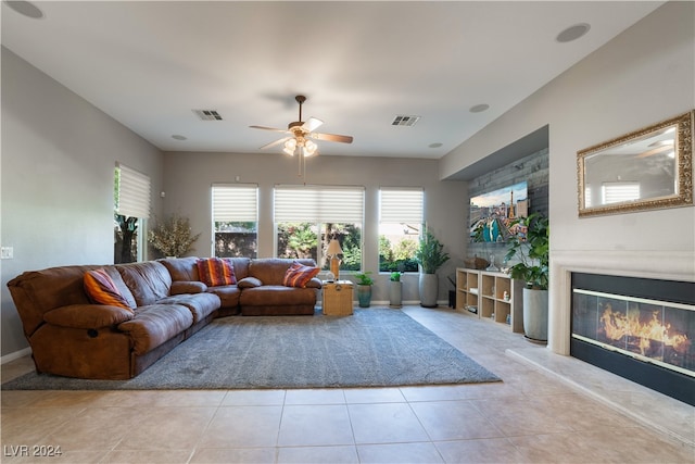 living area with a glass covered fireplace, light tile patterned floors, visible vents, and ceiling fan