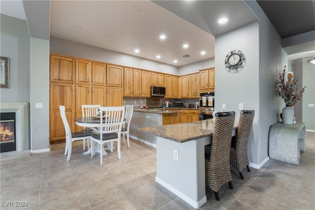 kitchen with light tile patterned floors, stone counters, a peninsula, appliances with stainless steel finishes, and a glass covered fireplace