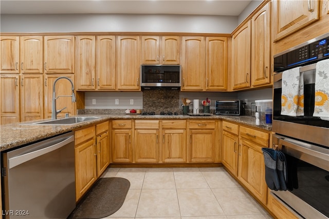 kitchen featuring light tile patterned floors, stone countertops, appliances with stainless steel finishes, and a sink