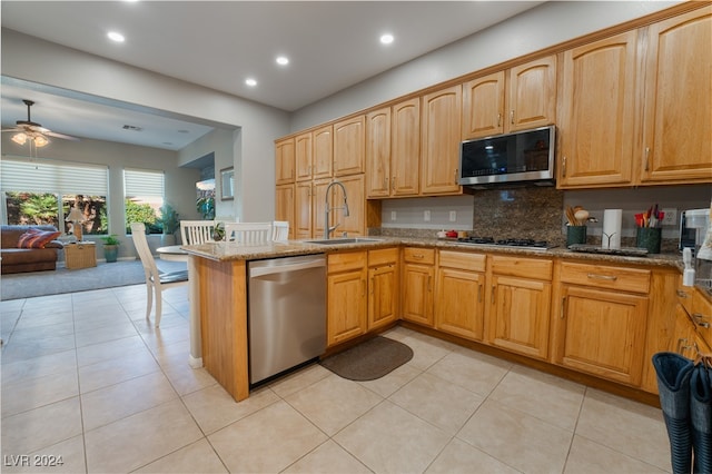 kitchen with light stone countertops, open floor plan, appliances with stainless steel finishes, a peninsula, and a sink