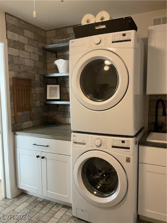 washroom featuring stacked washing maching and dryer, cabinets, and sink