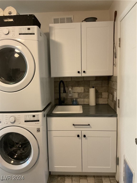 laundry area with stacked washing maching and dryer, cabinets, and sink