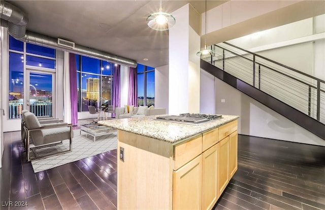 kitchen featuring dark hardwood / wood-style floors, a center island, light stone countertops, stainless steel gas cooktop, and light brown cabinetry