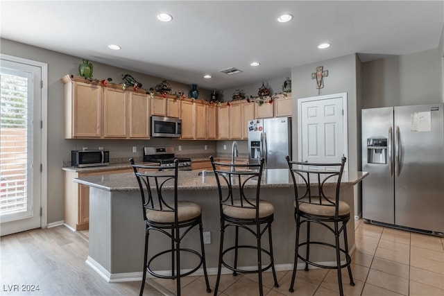 kitchen featuring light stone counters, a center island, a breakfast bar area, light wood-type flooring, and appliances with stainless steel finishes