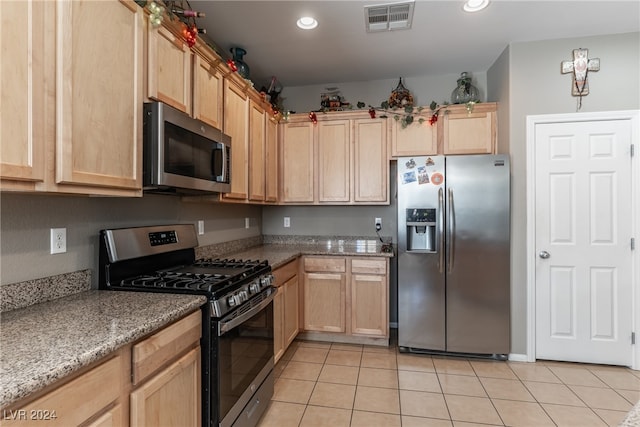 kitchen with stainless steel appliances, light tile patterned floors, light brown cabinetry, and light stone countertops