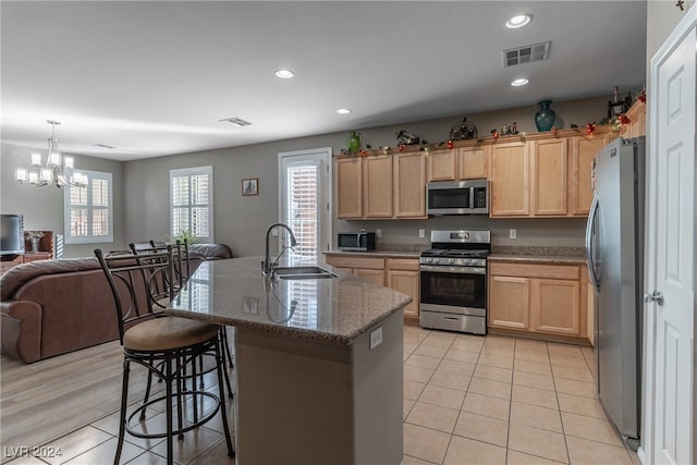 kitchen featuring light stone counters, stainless steel appliances, an inviting chandelier, sink, and a kitchen island with sink