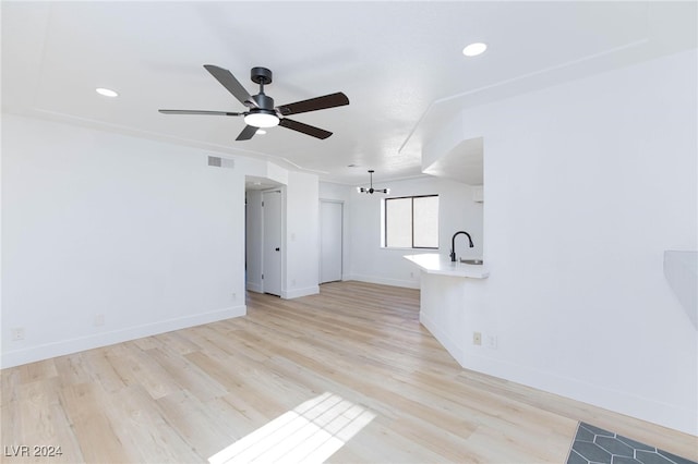 unfurnished living room featuring light wood-type flooring, sink, and ceiling fan with notable chandelier