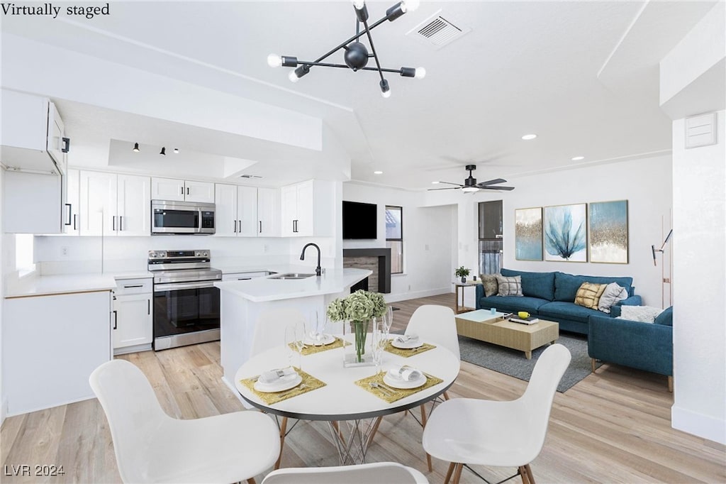 dining area featuring sink, light hardwood / wood-style floors, and ceiling fan with notable chandelier