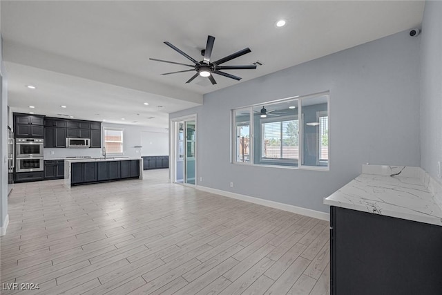 unfurnished living room featuring sink, light wood-type flooring, a wealth of natural light, and ceiling fan