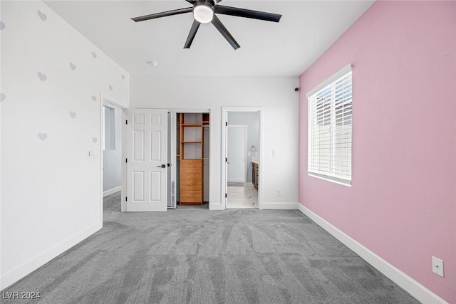 unfurnished bedroom featuring light carpet, ensuite bathroom, ceiling fan, a spacious closet, and a closet