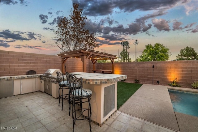 patio terrace at dusk with a pergola, grilling area, an outdoor bar, and exterior kitchen