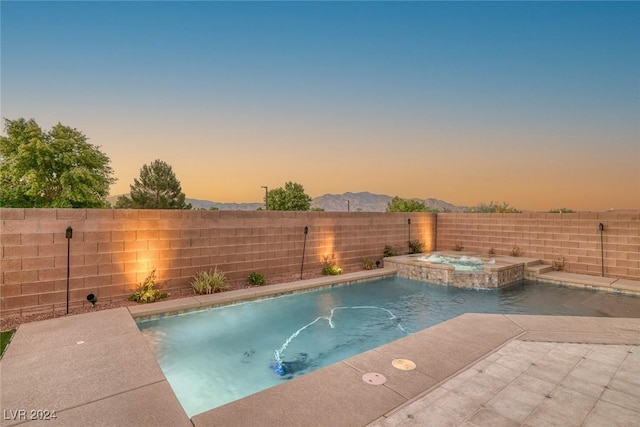 pool at dusk with an in ground hot tub, a mountain view, and pool water feature