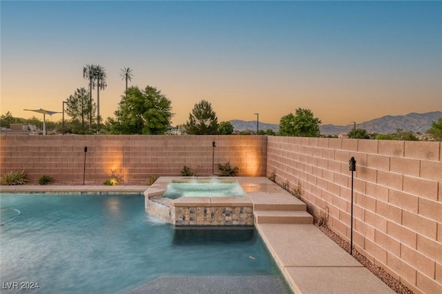 pool at dusk with a mountain view, pool water feature, and an in ground hot tub