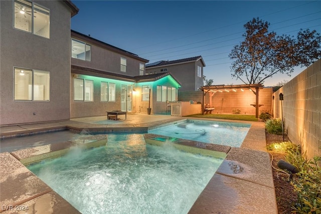 pool at dusk featuring pool water feature, an outdoor kitchen, a pergola, and a patio