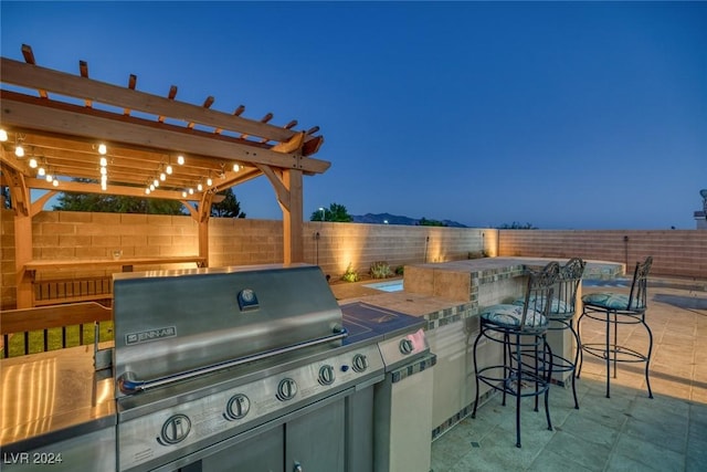 patio terrace at dusk featuring a pergola, area for grilling, and a bar