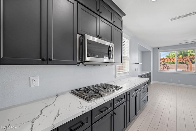 kitchen with ceiling fan, light stone counters, light wood-type flooring, and appliances with stainless steel finishes