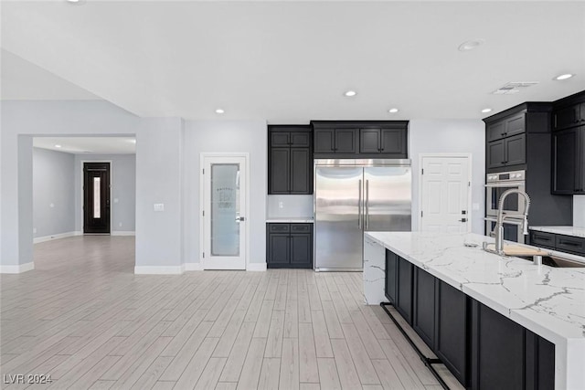 kitchen featuring light stone countertops, stainless steel appliances, light hardwood / wood-style flooring, and sink