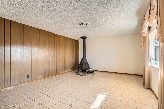 unfurnished room with a textured ceiling, a wood stove, and wood walls