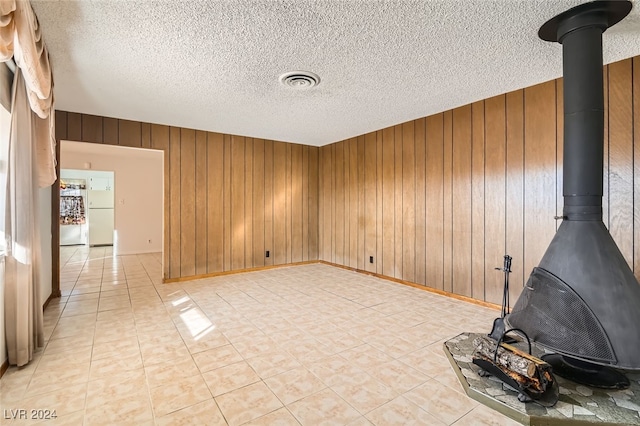 empty room with wood walls, a wood stove, and a textured ceiling