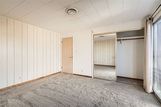 unfurnished bedroom featuring carpet floors, a closet, and wooden walls