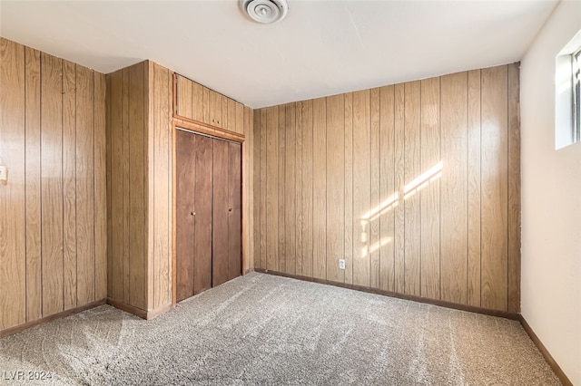 unfurnished bedroom featuring carpet flooring, wooden walls, and a closet