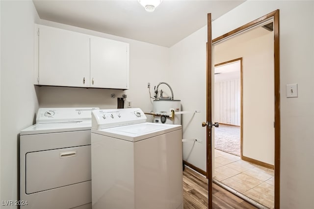 clothes washing area featuring washing machine and dryer, water heater, light hardwood / wood-style flooring, and cabinets