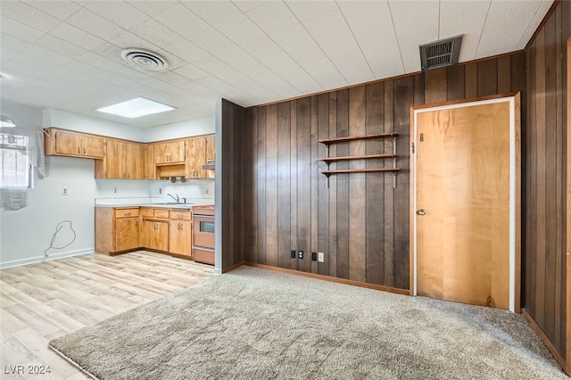 kitchen with sink, stainless steel stove, light hardwood / wood-style floors, and wood walls