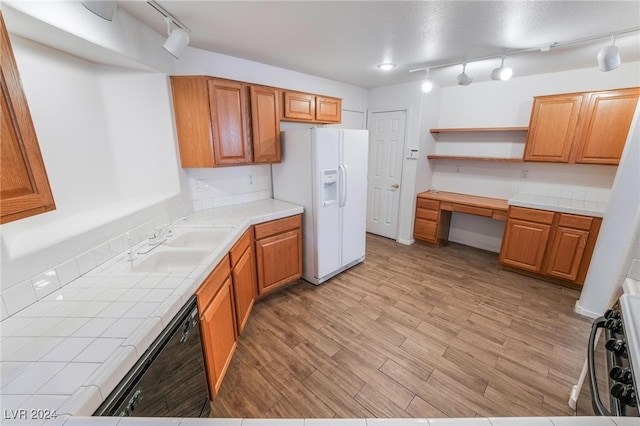 kitchen featuring light hardwood / wood-style floors, tile countertops, sink, white refrigerator with ice dispenser, and black dishwasher