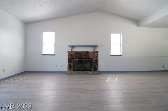 unfurnished living room with a stone fireplace, hardwood / wood-style flooring, lofted ceiling, and a textured ceiling