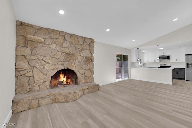 unfurnished living room featuring lofted ceiling, sink, light hardwood / wood-style flooring, and a stone fireplace