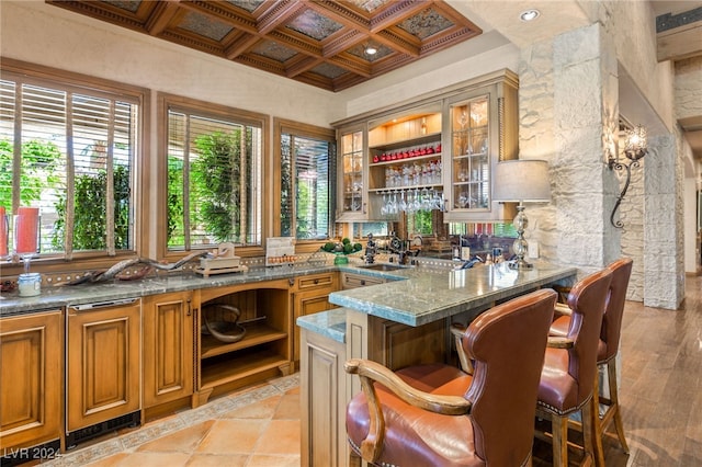 bar with sink, coffered ceiling, beam ceiling, light hardwood / wood-style flooring, and dark stone countertops