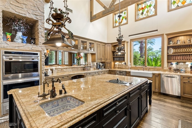 kitchen with wood-type flooring, light stone counters, appliances with stainless steel finishes, sink, and a high ceiling