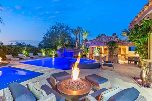 pool at dusk with an outdoor living space with a fire pit, pool water feature, and a patio area