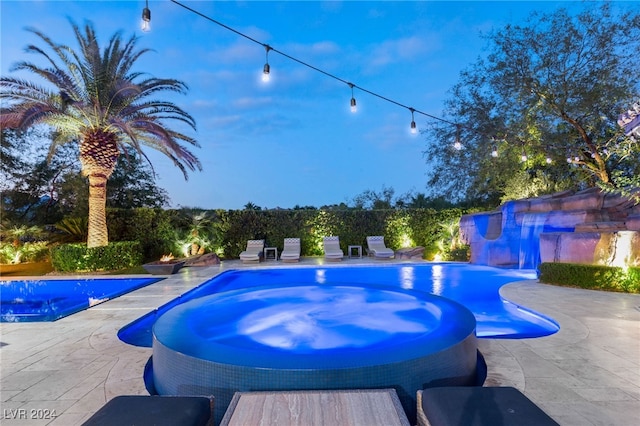 pool at dusk with a patio area and an in ground hot tub