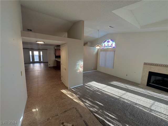 unfurnished living room with a textured ceiling, ceiling fan, dark colored carpet, lofted ceiling, and a tiled fireplace