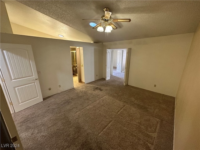 empty room featuring lofted ceiling, ceiling fan, carpet floors, and a textured ceiling