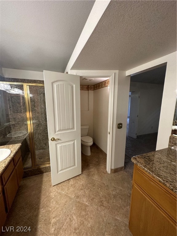 bathroom with tile patterned floors, vanity, a textured ceiling, toilet, and a shower with shower door