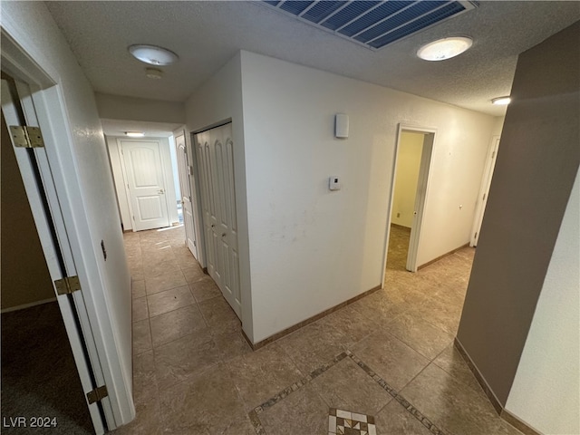 hall featuring light tile patterned floors and a textured ceiling