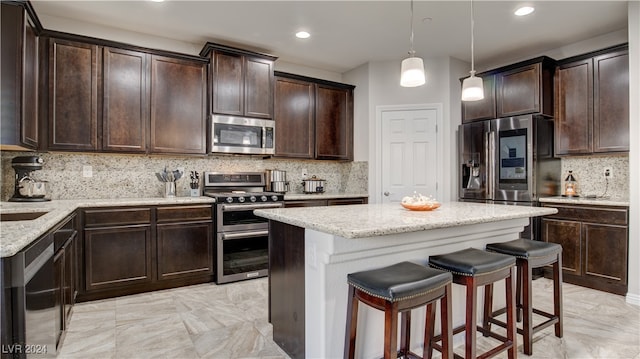 kitchen featuring appliances with stainless steel finishes, decorative light fixtures, a center island, light stone counters, and dark brown cabinets