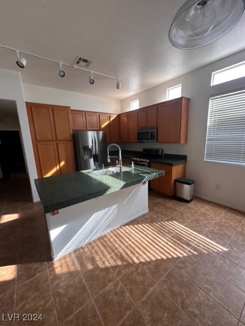 kitchen with rail lighting, sink, stainless steel appliances, and a kitchen island with sink