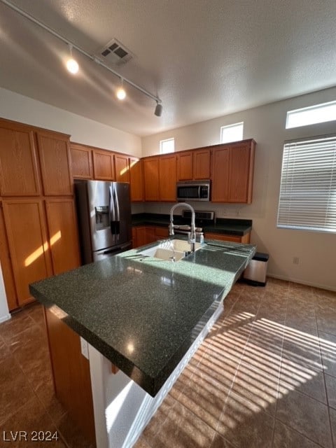 kitchen with track lighting, a center island with sink, sink, a textured ceiling, and appliances with stainless steel finishes