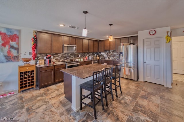 kitchen with decorative light fixtures, a breakfast bar area, stainless steel appliances, visible vents, and backsplash