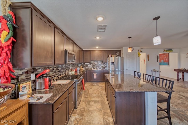 kitchen featuring a breakfast bar area, stainless steel appliances, a kitchen island, visible vents, and tasteful backsplash