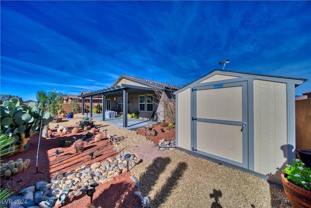 rear view of property featuring fence, a storage unit, a patio, and an outbuilding