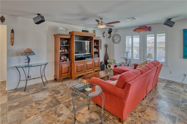 living area with ceiling fan, stone finish floor, visible vents, and baseboards