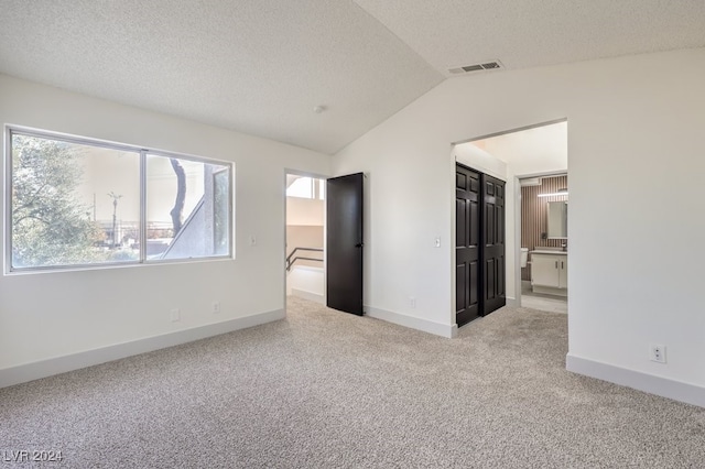 unfurnished bedroom with a textured ceiling, connected bathroom, light carpet, and vaulted ceiling